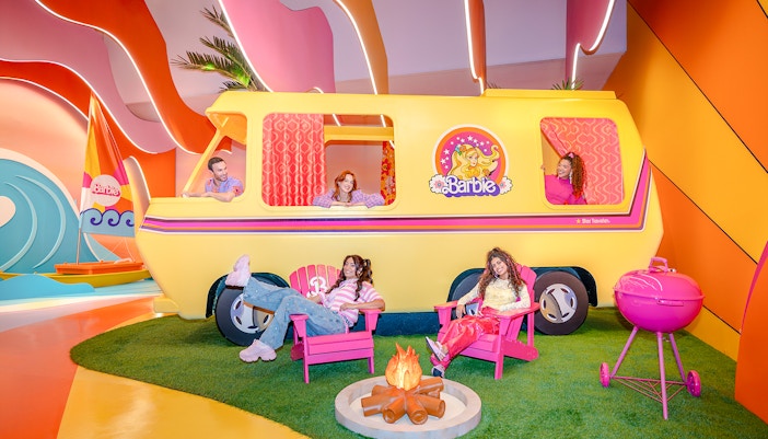 Barbie Malibu van with people relaxing in chairs and a campfire nearby.