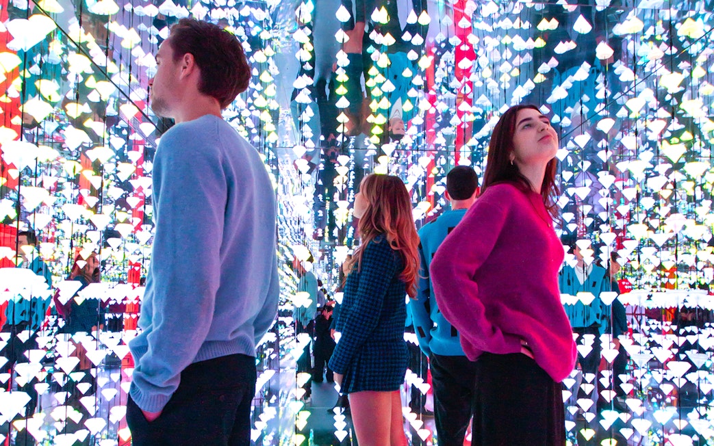 Tourists viewing colorful light installation at Moco Museum, Amsterdam, with Banksy artworks.