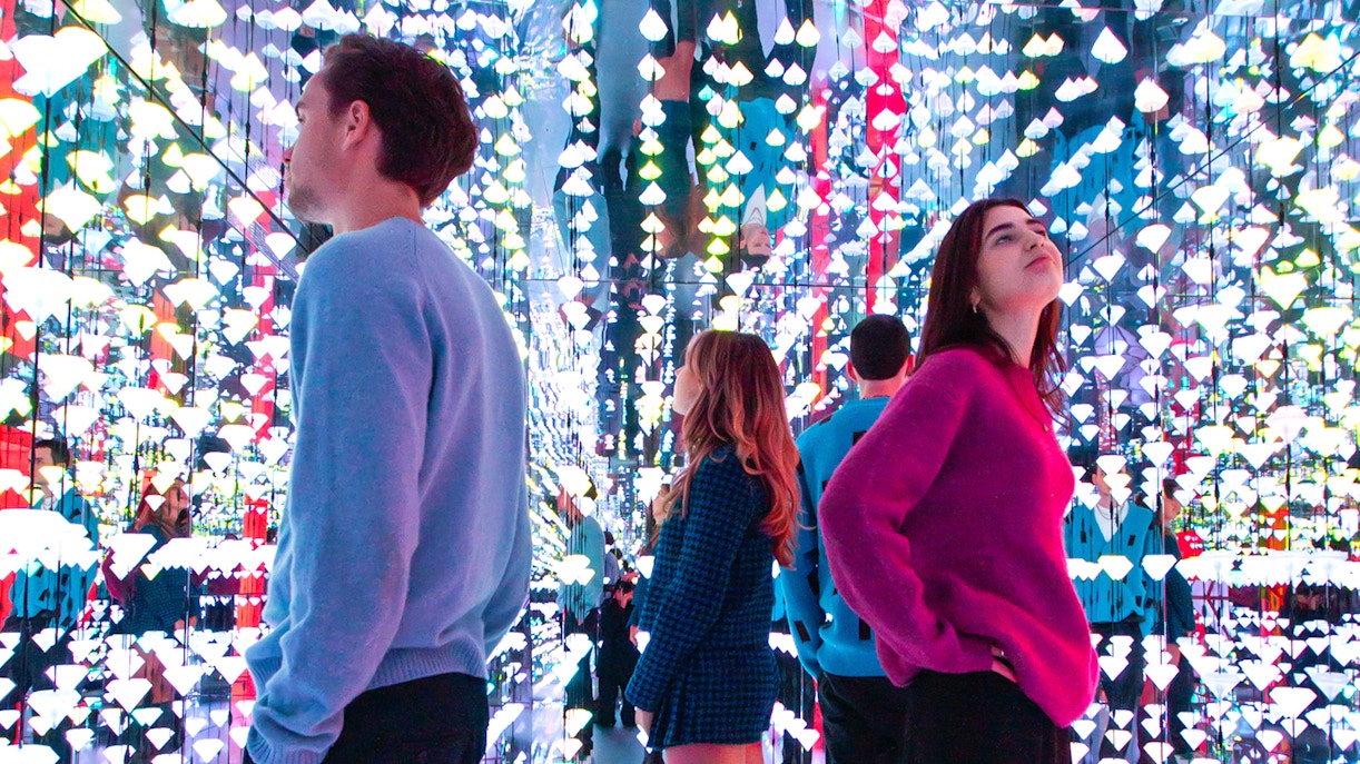 Tourists viewing colorful light installation at Moco Museum, Amsterdam, with Banksy artworks.