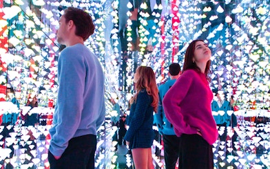 Tourists viewing colorful light installation at Moco Museum, Amsterdam, with Banksy artworks.