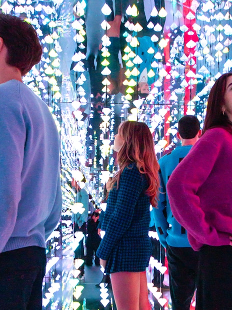 Tourists viewing colorful light installation at Moco Museum, Amsterdam, with Banksy artworks.