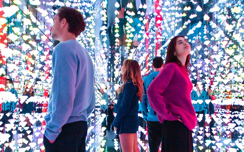 Tourists viewing colorful light installation at Moco Museum, Amsterdam, with Banksy artworks.