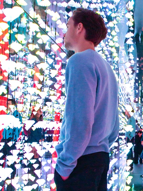 Tourists viewing colorful light installation at Moco Museum, Amsterdam, with Banksy artworks.
