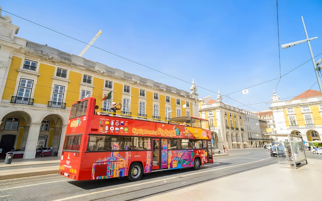 Lisbon hop-on hop-off bus at Praca do Comercio with yellow buildings in background.