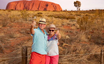 Couple toasting with champagne in front of Uluru during sunset on a tour from Alice Springs.