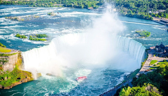 Visitors on a boat tour approaching the base of Niagara Falls in the summer, with mist rising from the cascading water.