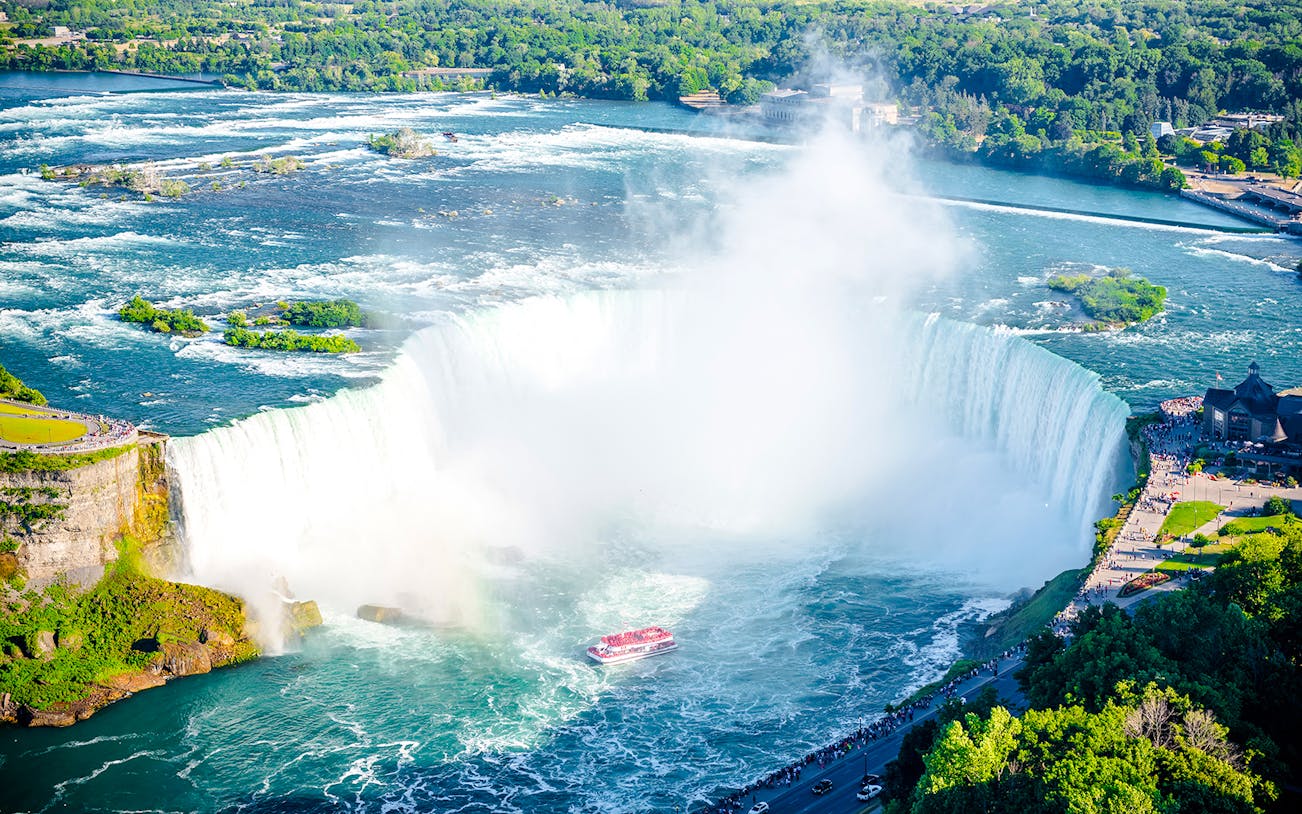 Niagara Falls with tour boat in summer, surrounded by lush greenery.