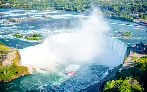 Niagara Falls with tour boat in summer, surrounded by lush greenery.