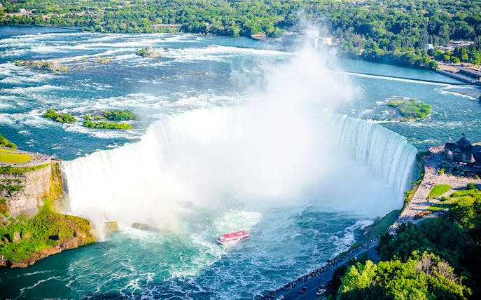 Niagara Falls with tour boat in summer, surrounded by lush greenery.