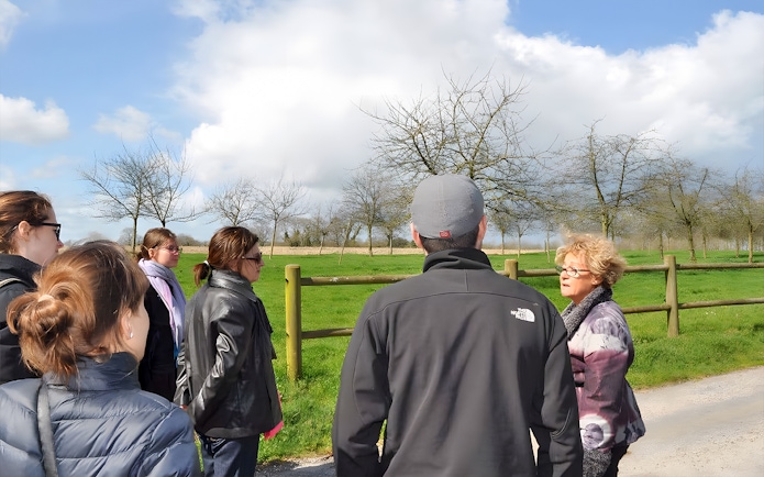 Tour group listening to a guide at Normandy, France, with green fields and trees in the background.