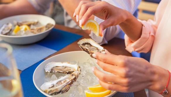 Tour group enjoying fresh oysters with lemon on Bruny Island coastline.