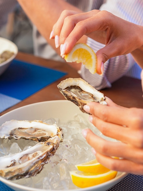 Tour group enjoying fresh oysters with lemon on Bruny Island coastline.