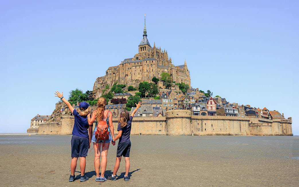 Visitors admire Mont Saint-Michel from the sandy shore, Normandy, France.