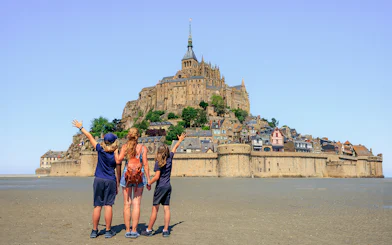 Visitors admire Mont Saint-Michel from the sandy shore, Normandy, France.