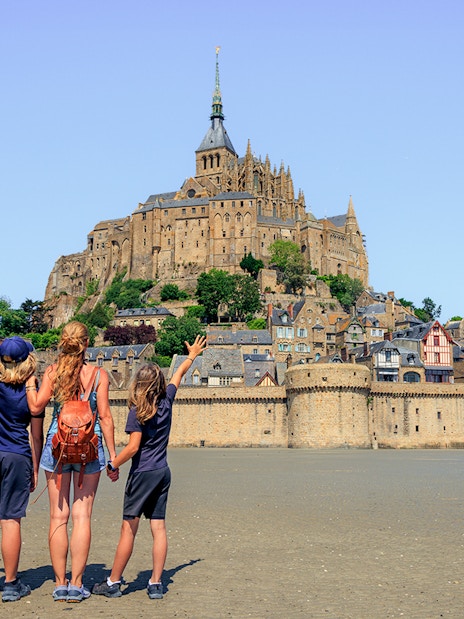 Visitors admire Mont Saint-Michel from the sandy shore, Normandy, France.