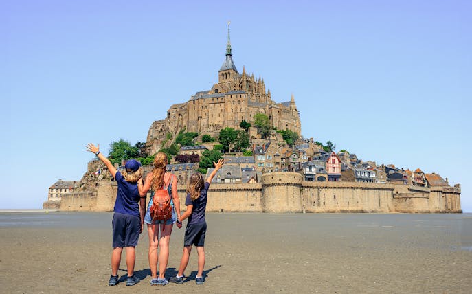 Visitors admire Mont Saint-Michel from the sandy shore, Normandy, France.