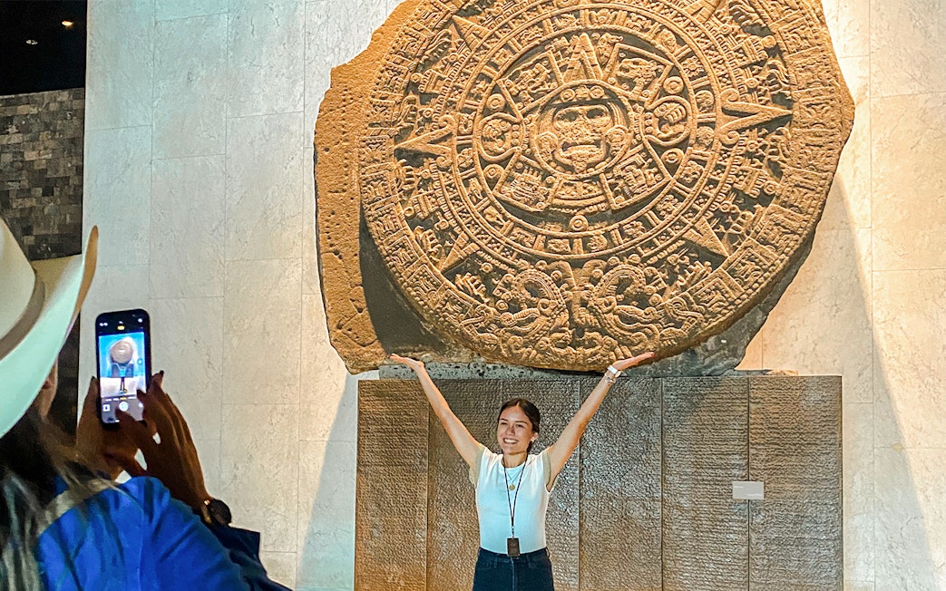 Stone Aztec calendar at the Anthropology Museum, Mexico, with a visitor posing in front.