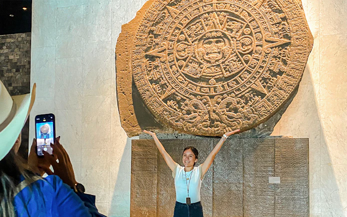 Stone Aztec calendar at the Anthropology Museum, Mexico, with a visitor posing in front.