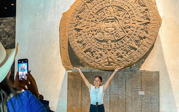 Stone Aztec calendar at the Anthropology Museum, Mexico, with a visitor posing in front.