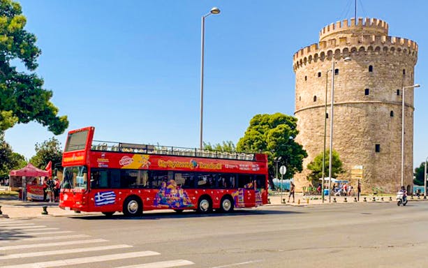 Red double-decker bus near the White Tower on Thessaloniki Hop-On-Hop-Off Tour.