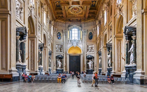Interior of the Basilica of Saint John in Lateran with ornate columns and visitors seated.