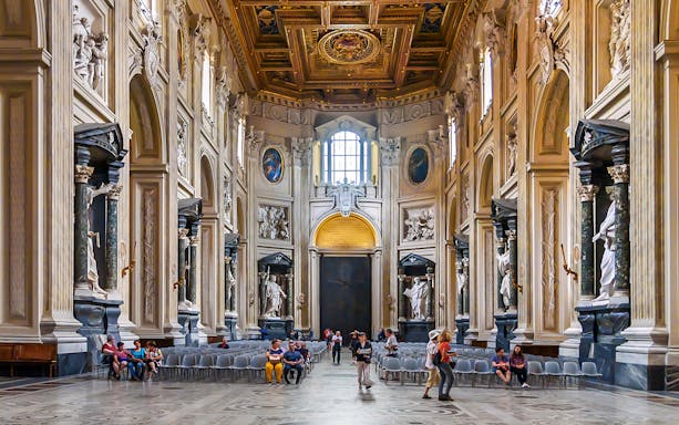Interior of the Basilica of Saint John in Lateran with ornate columns and visitors seated.