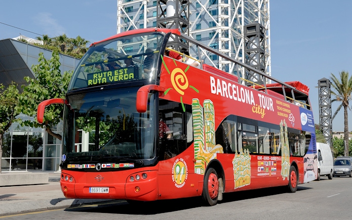 Barcelona tour bus parked near modern architecture on a sunny day.