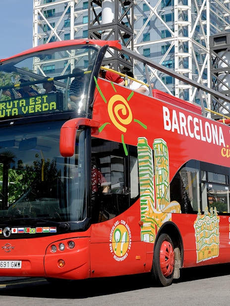 Barcelona tour bus parked near modern architecture on a sunny day.