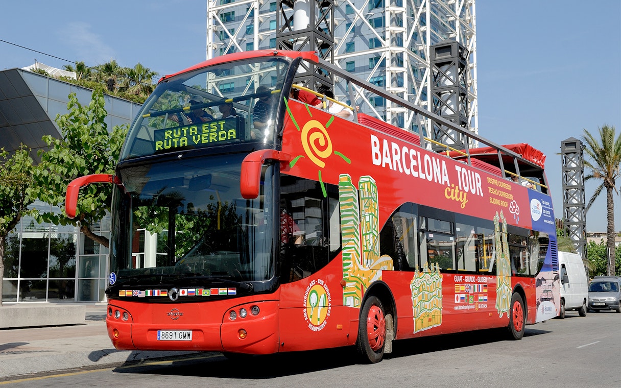 Barcelona tour bus parked near modern architecture on a sunny day.