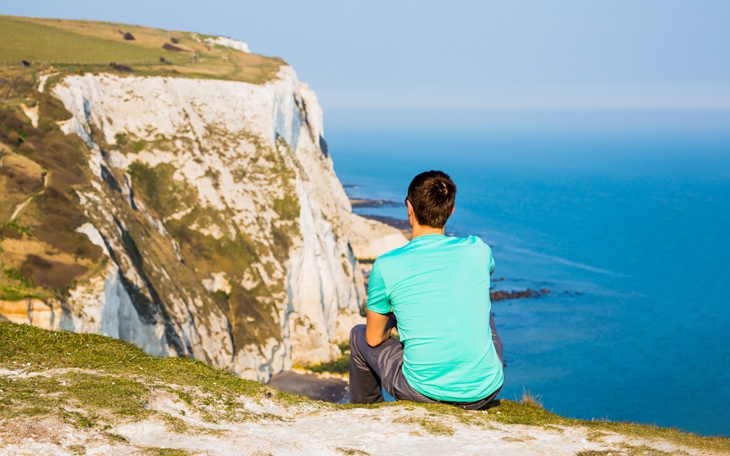 Person sitting on cliff overlooking the White Cliffs of Dover, England.
