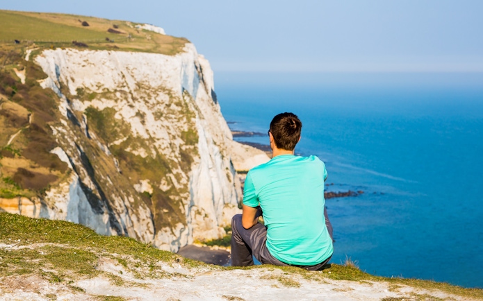Person sitting on cliff overlooking the White Cliffs of Dover, England.