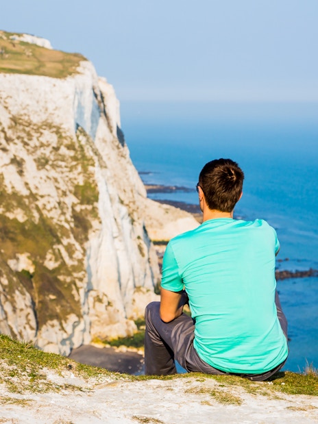 Person sitting on cliff overlooking the White Cliffs of Dover, England.