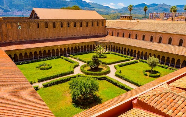 Cloister garden of Monreale Cathedral, Sicily, with arches and greenery.