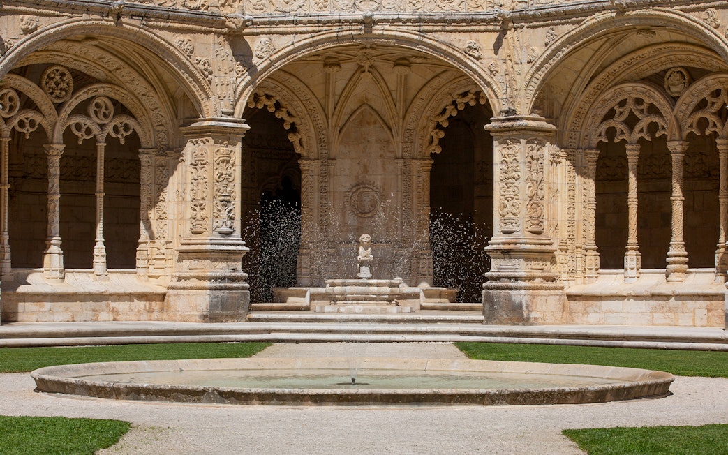 Jerónimos Monastery cloister with ornate arches and central fountain in Lisbon.