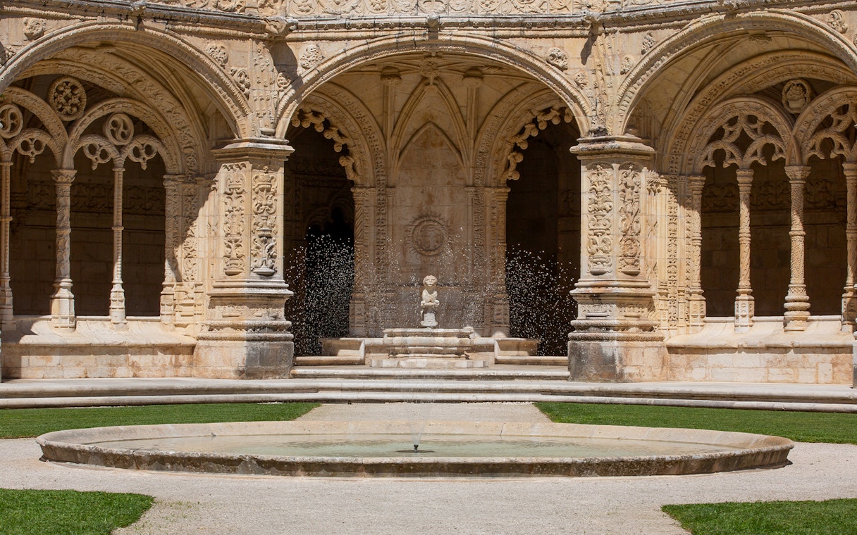 Jerónimos Monastery cloister with ornate arches and central fountain in Lisbon.