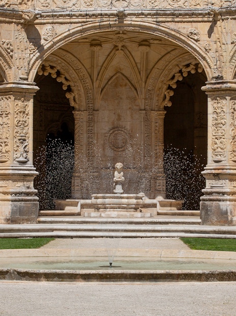 Jerónimos Monastery cloister with ornate arches and central fountain in Lisbon.