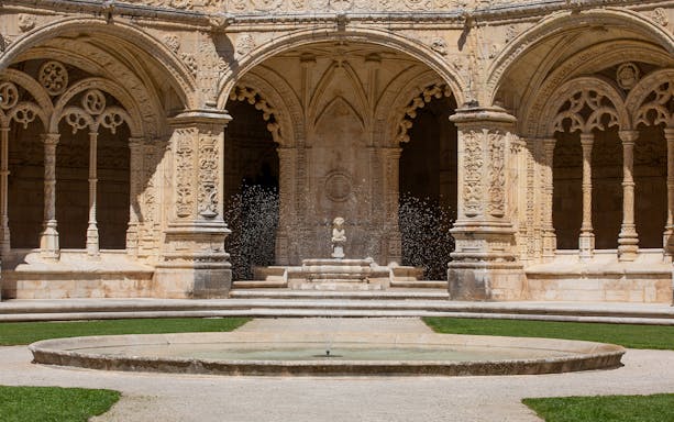 Jerónimos Monastery cloister with ornate arches and central fountain in Lisbon.
