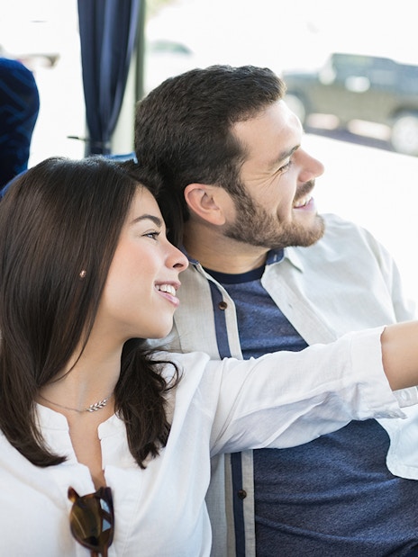 Couple smiling and pointing out the window on a bus tour.