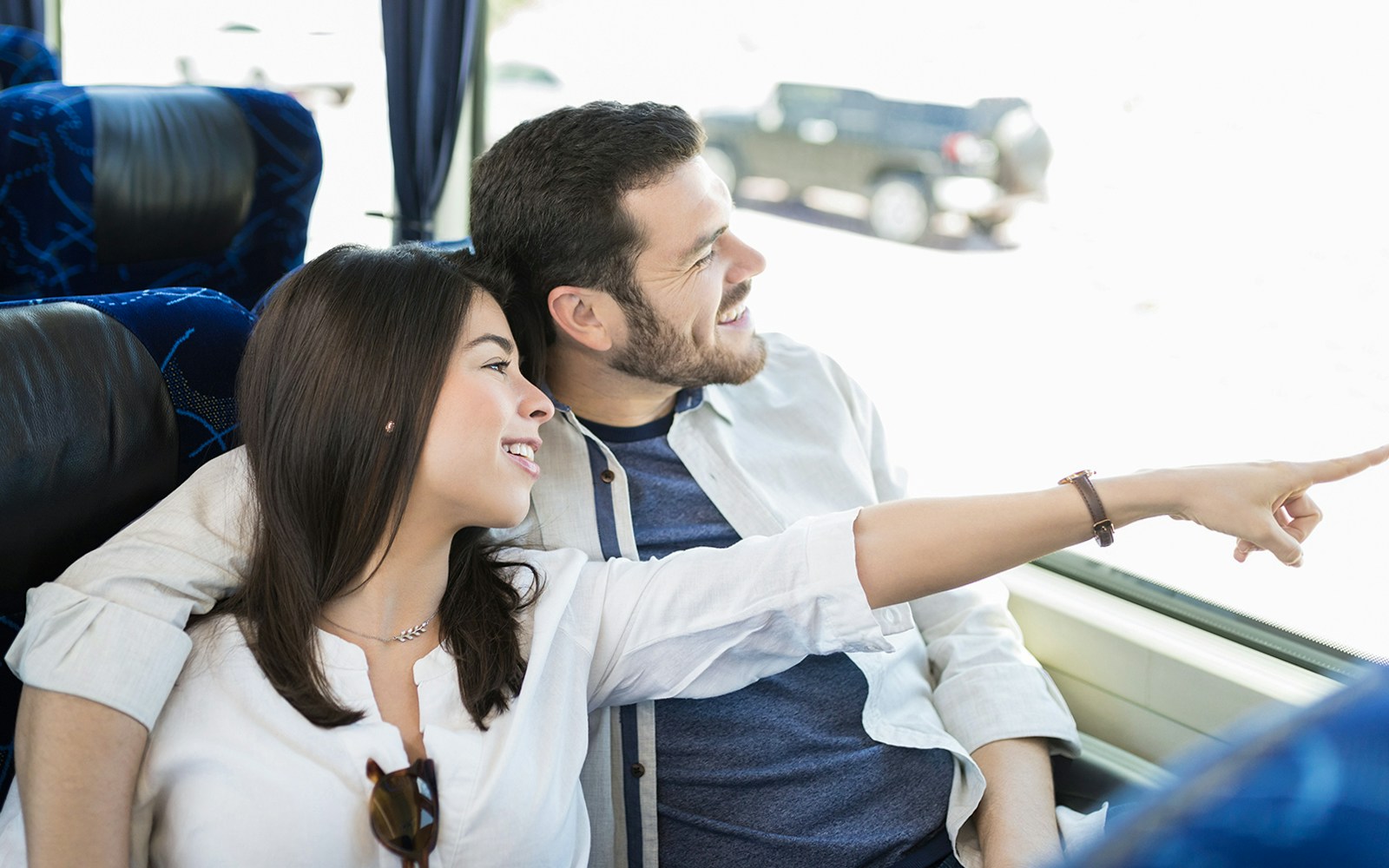 Couple smiling and pointing out the window on a bus tour.