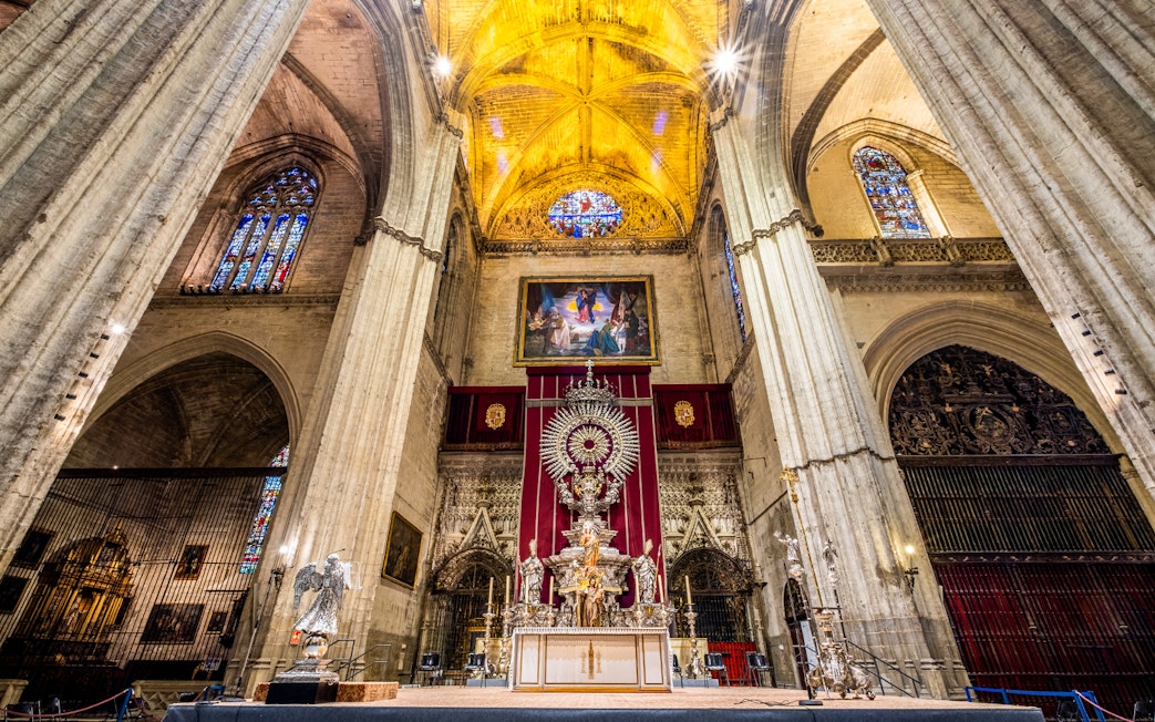 Interior of Seville Cathedral with ornate altar and stained glass windows, part of Exclusive Cathedral & Giralda Tour.