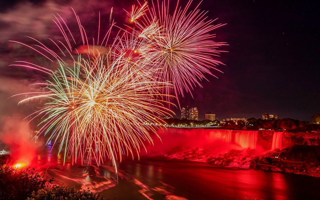 Fireworks display over illuminated Niagara Falls at night.