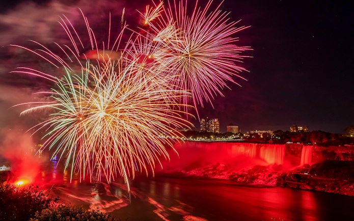 Fireworks display over illuminated Niagara Falls at night.