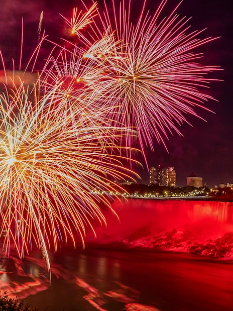 Fireworks display over illuminated Niagara Falls at night.