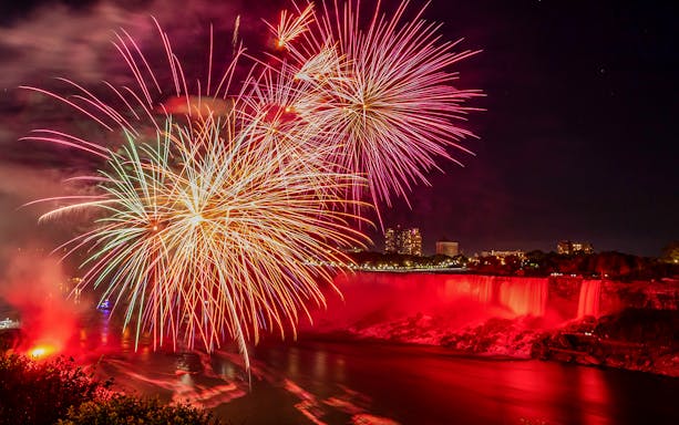 Fireworks display over illuminated Niagara Falls at night.