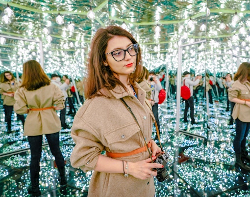 Woman exploring a mirror labyrinth with reflections and lights.