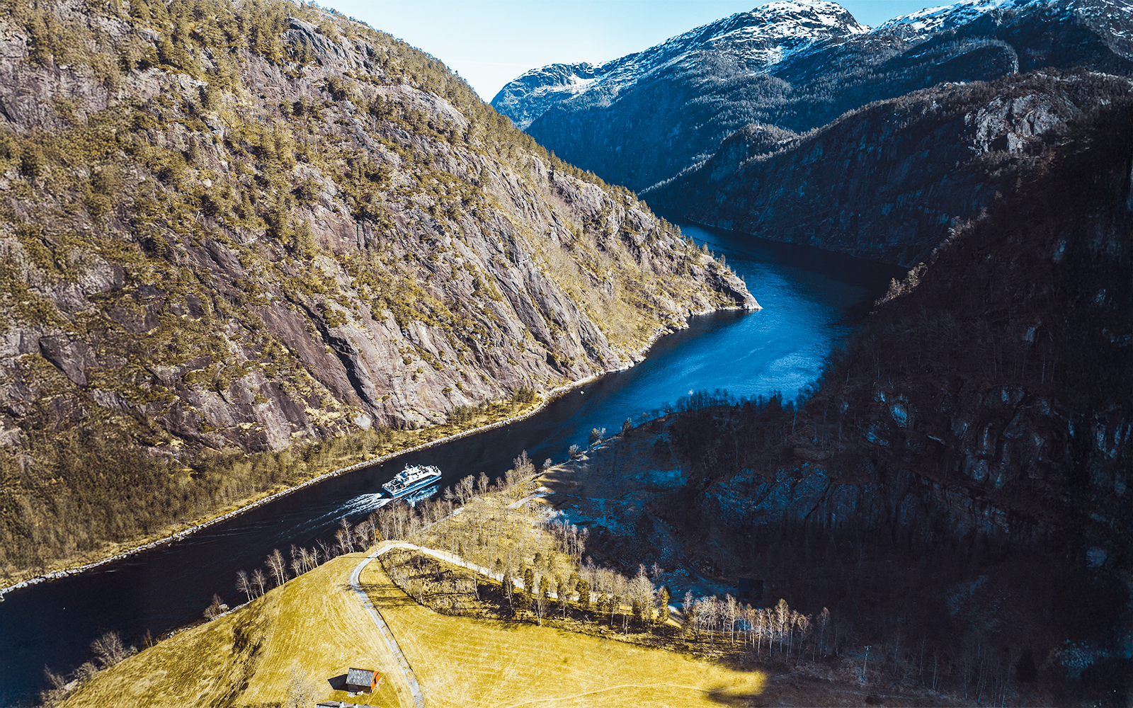 Aerial view of a cruise ship navigating Mostraumen Fjord, surrounded by steep cliffs and blue water.