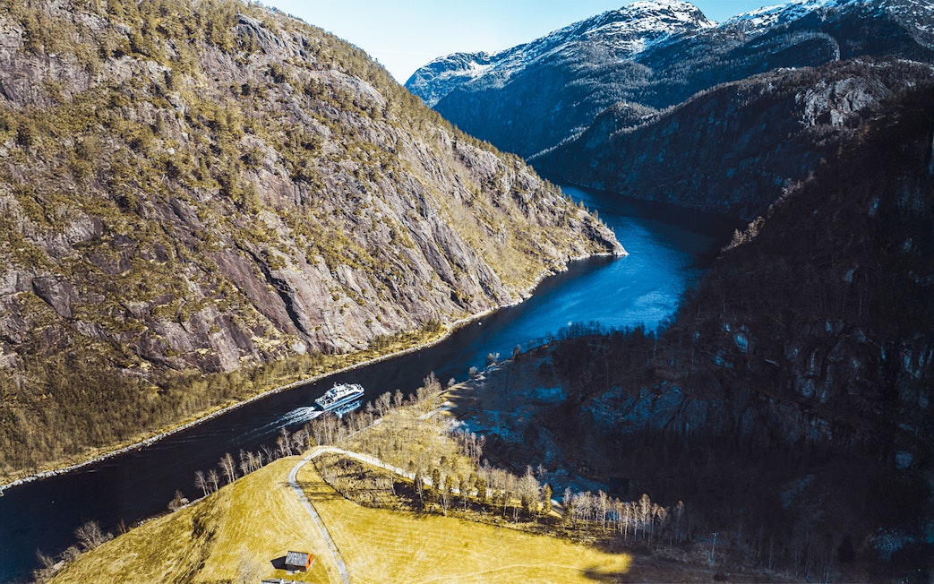 Aerial view of a cruise ship navigating Mostraumen Fjord, surrounded by steep cliffs and blue water.