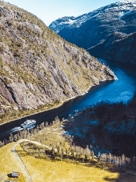 Aerial view of a cruise ship navigating Mostraumen Fjord, surrounded by steep cliffs and blue water.