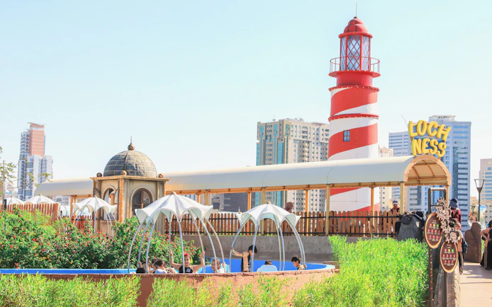 Lochness spinboat ride at Al Montazah Parks, Island of Legends with lighthouse and cityscape.