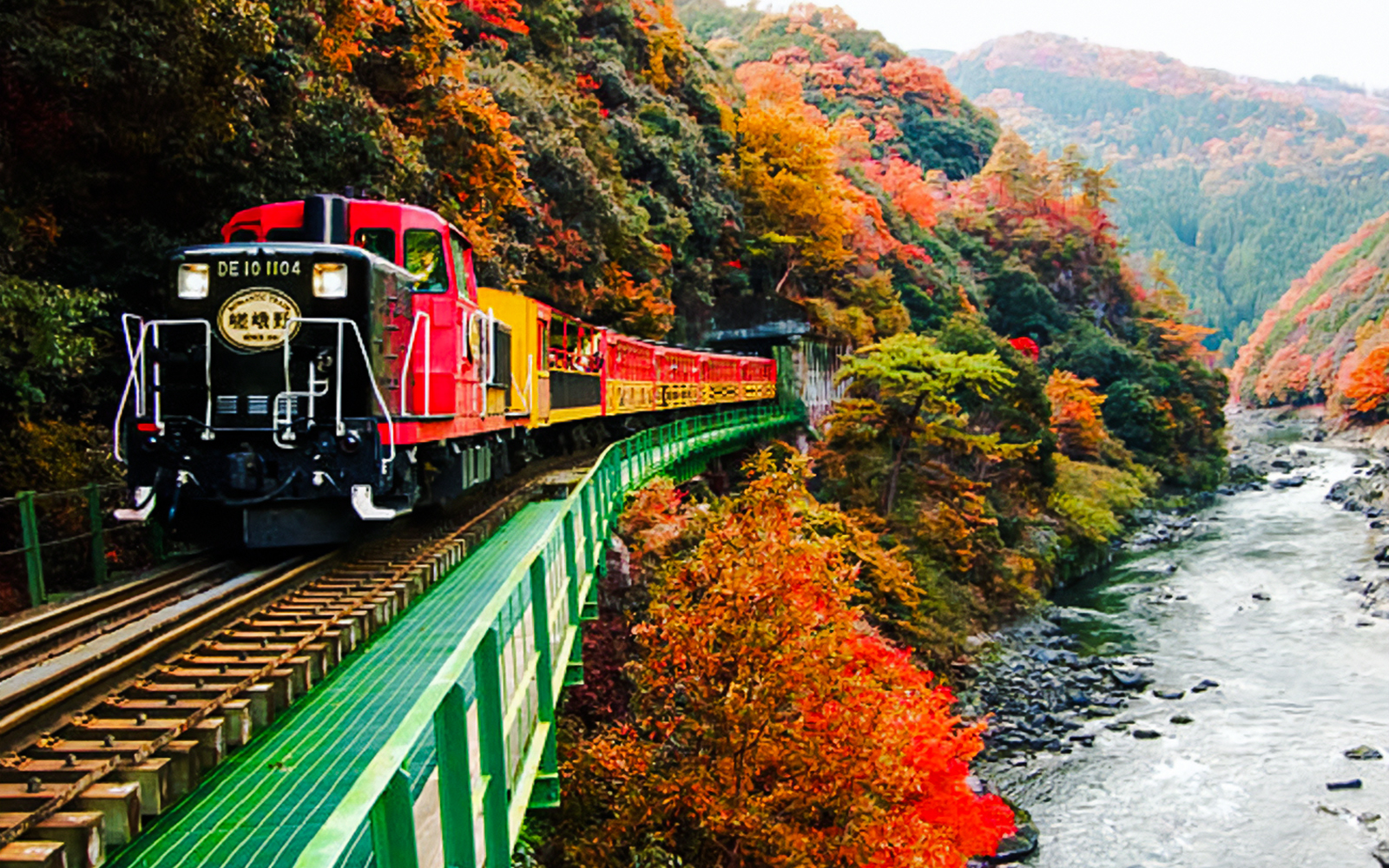 Sagano Romantic Train crossing a bridge through autumn foliage in Kyoto, Japan.